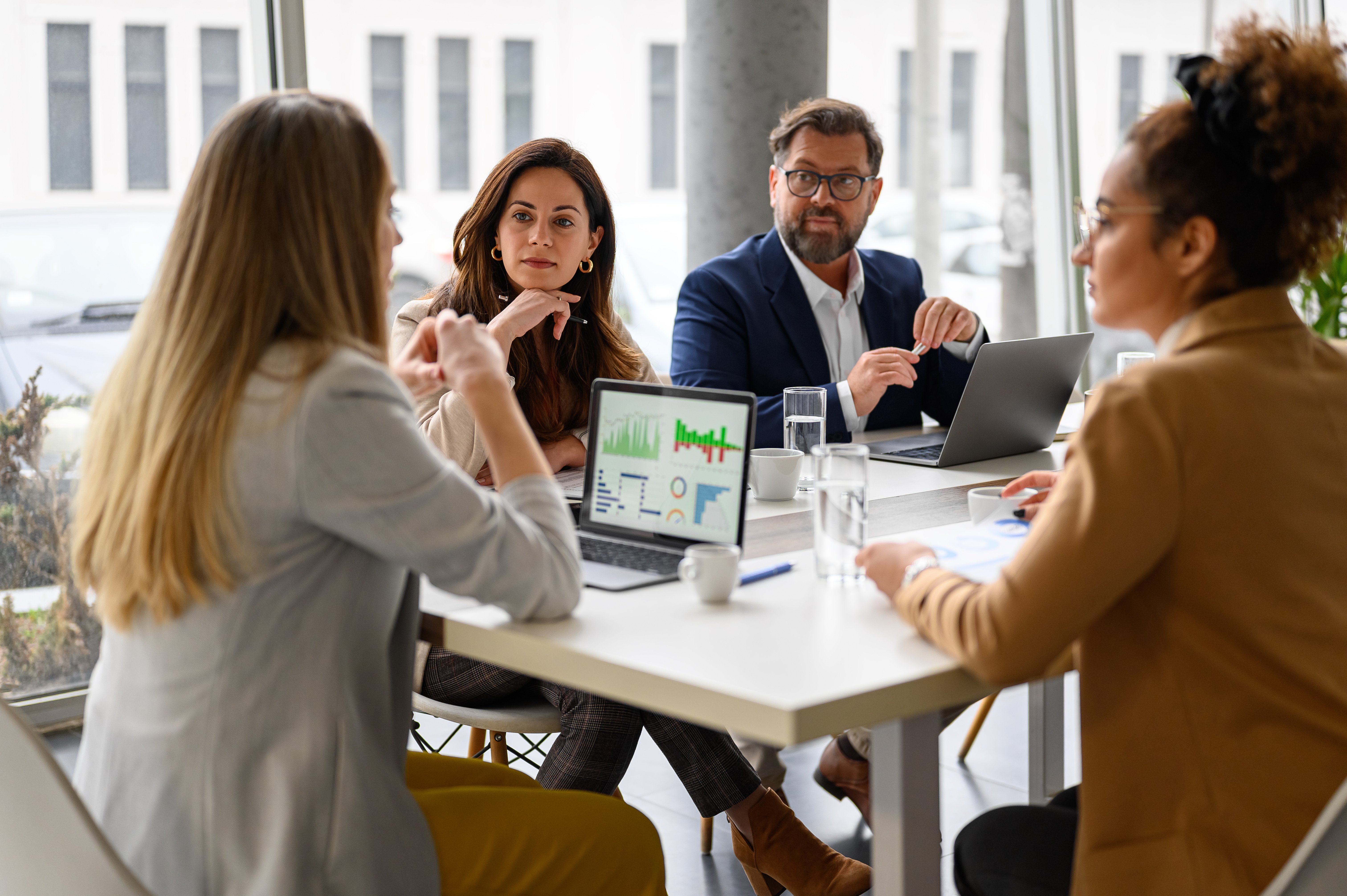 Businesswoman reviewing report on her laptop while discussing business growth with coworkers in meeting