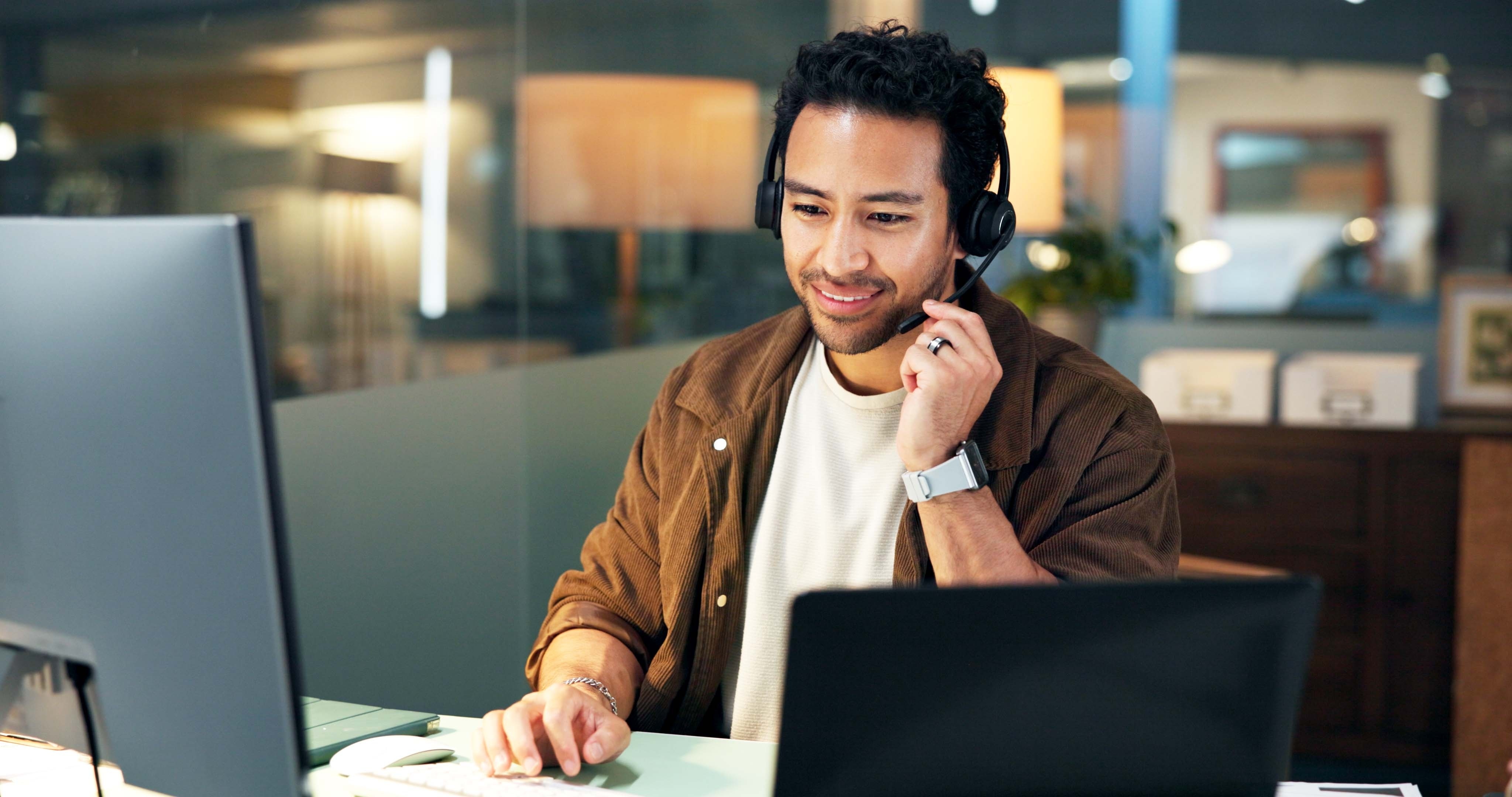 A man with a headset and a computer attending a virtual meeting