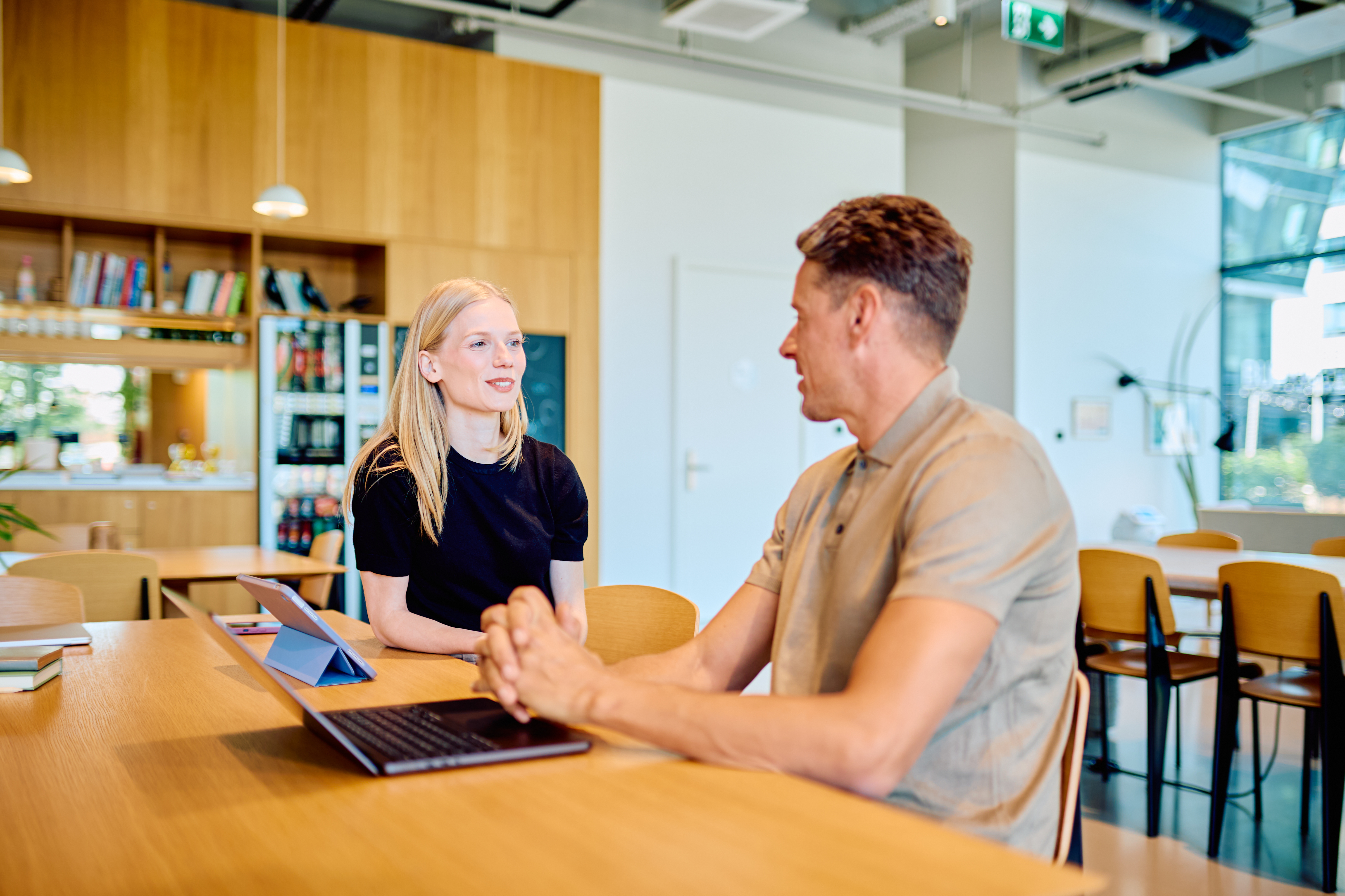 Business professionals collaborating at a wooden table with laptop and tablet, discussing strategy in a contemporary office